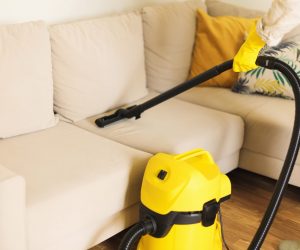 Woman cleaning sofa with yellow vacuum cleaner. Copy space. Clean concept.